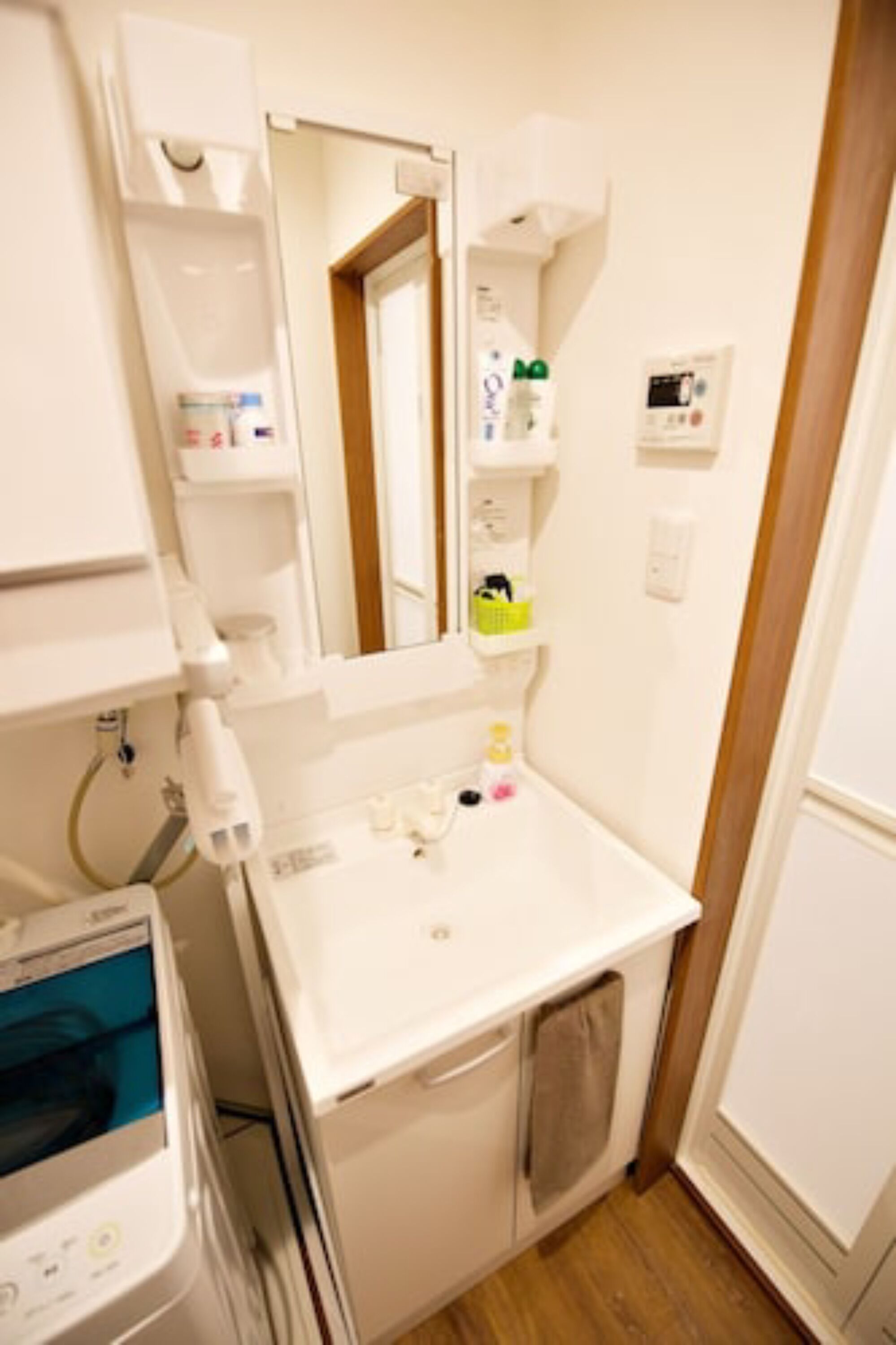 Un baño pequeño y limpio con lavamanos blanco, espejo y repisas con artículos de aseo.