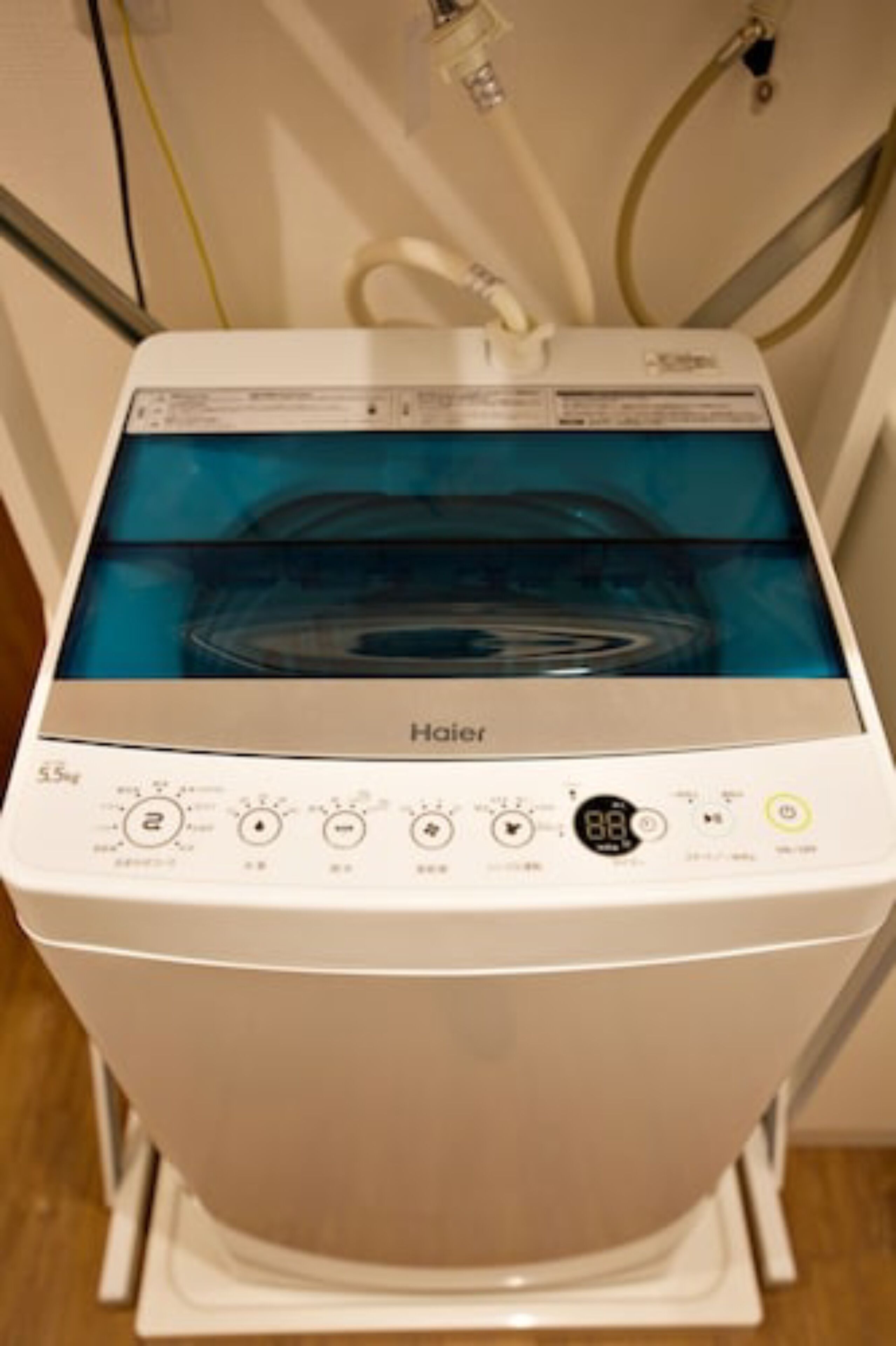 Un lave-linge Haier doté d’un écran numérique, d’un panneau de commande et d’un tuyau d’arrivée d’eau.