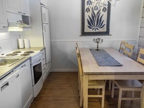 A compact kitchen with white appliances, a dining table with chairs, and a decorative wall piece. - Lepolinna b by Interhome (Nilsiä)
