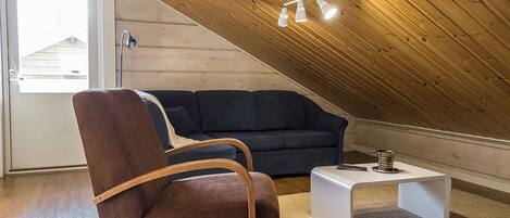A cozy living room with a sloped ceiling, a dark-colored sofa, a brown armchair, and a small white coffee table.