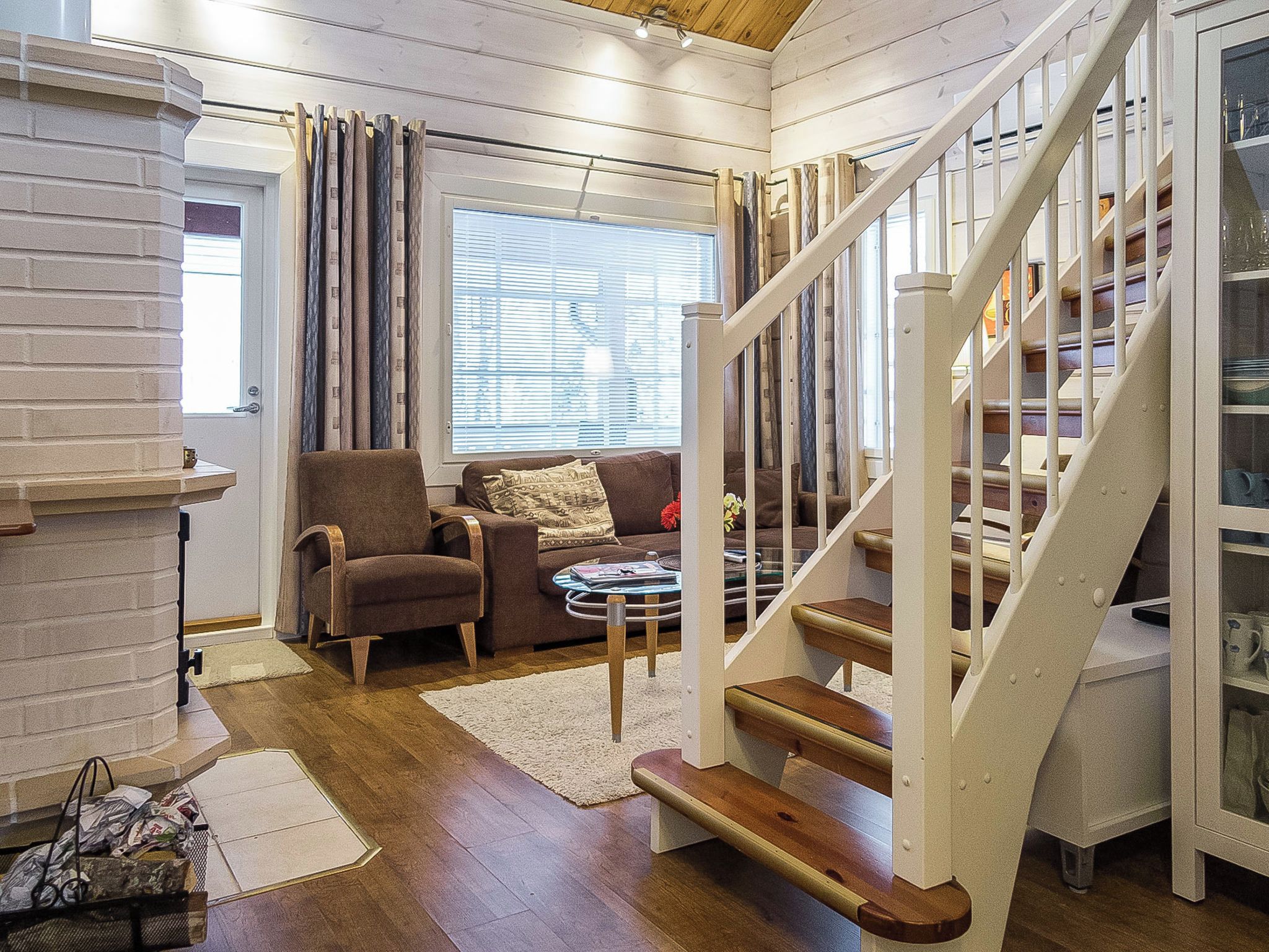 Een gezellige woonkamer met een houten trap, een open haard en een groot raam met luiken.