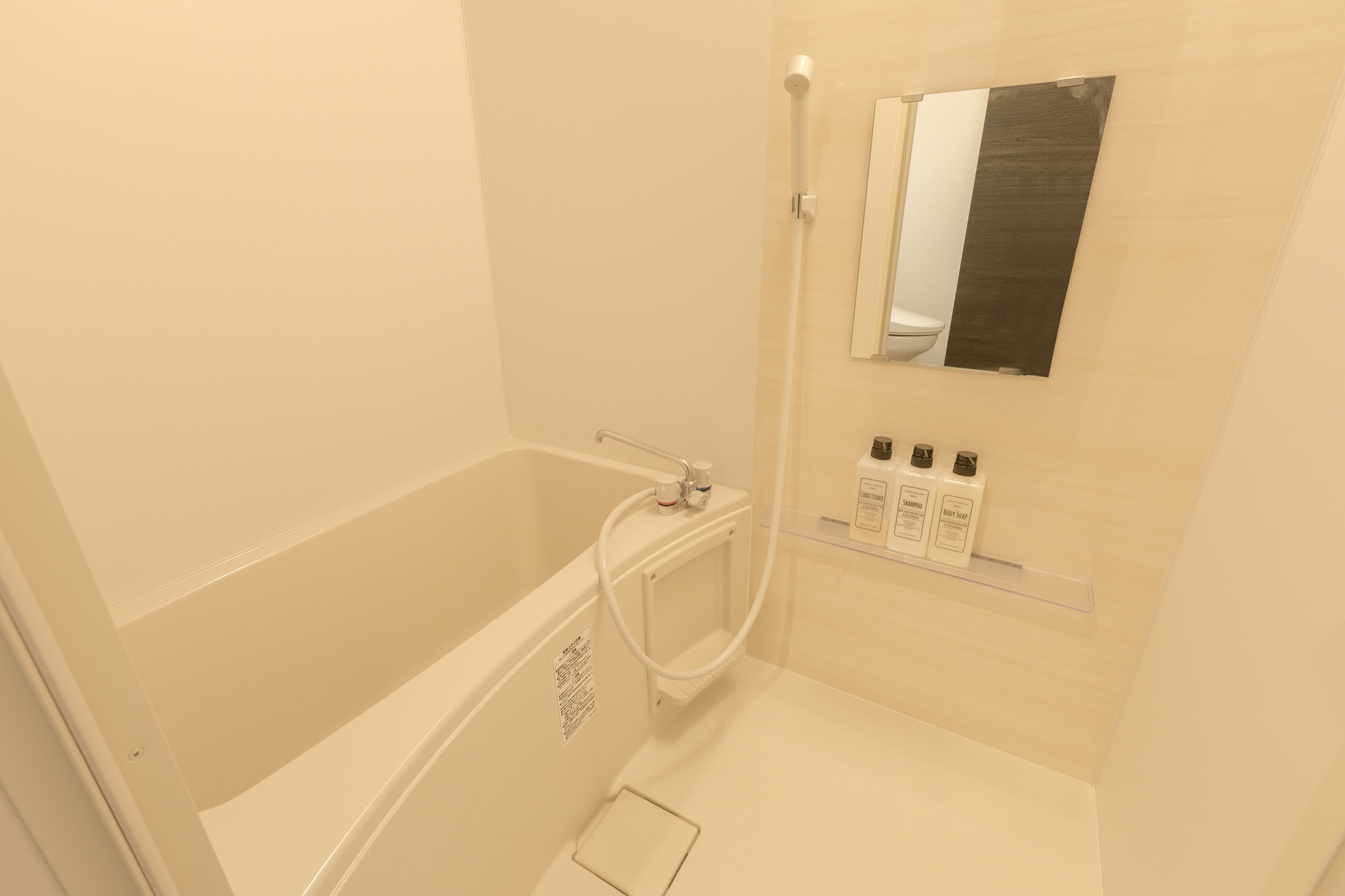 A modern bathroom with a bathtub, a shower, and a mirror. There are toiletries on a shelf.