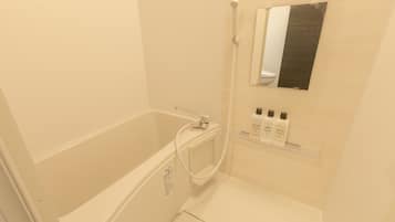 A modern bathroom with a bathtub, a shower, and a mirror. There are toiletries on a shelf.