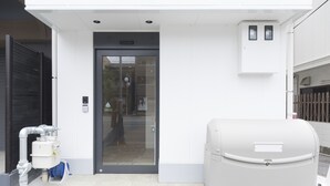 A building entrance with a glass door, a mailbox, and a water tank. - Rakuraku Inn Miyabi (Kyoto)