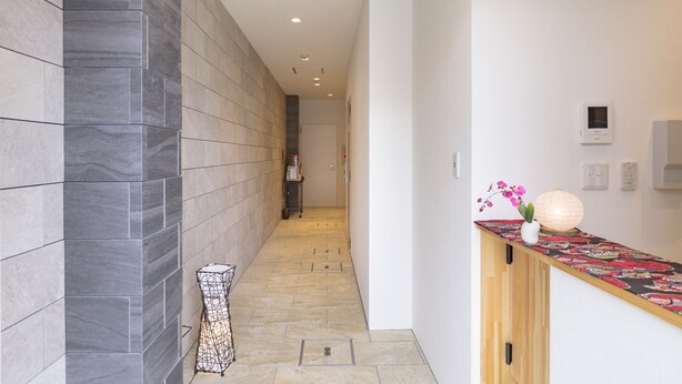 A hallway with a tiled floor, a wooden cabinet with a patterned countertop, and a small table with a vase of flowers. - Rakuraku Inn Miyabi (Kyoto)