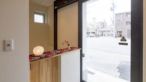 A reception area with a wooden counter, a decorative lamp, and a view of the street outside. - Rakuraku Inn Miyabi (Kyoto)