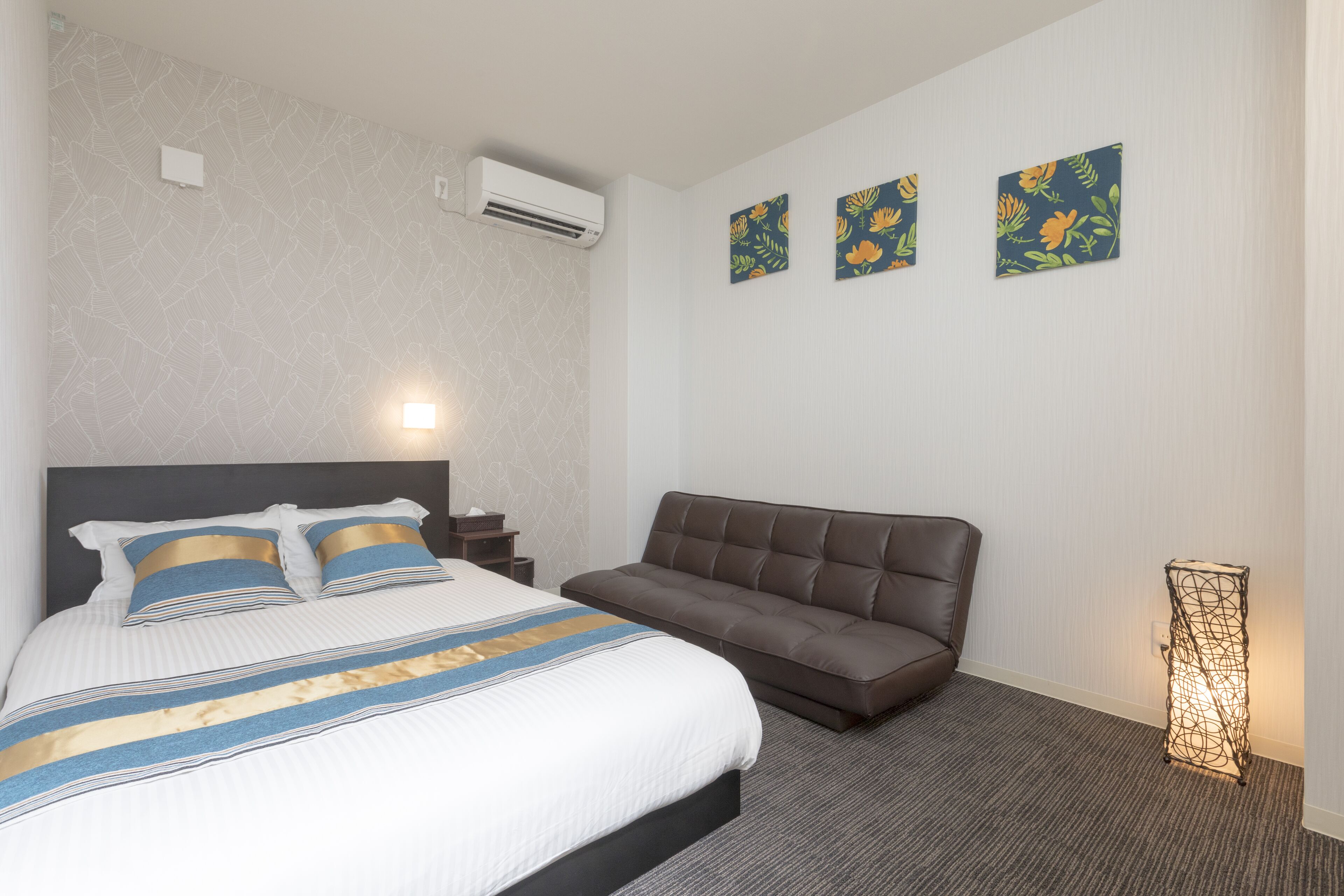 A hotel room with a large bed, a brown sofa, and three floral wall art pieces.