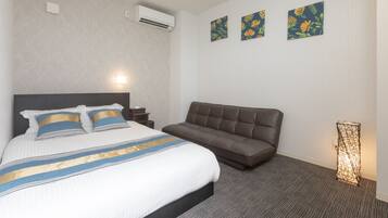 A hotel room with a large bed, a brown sofa, and three floral wall art pieces.