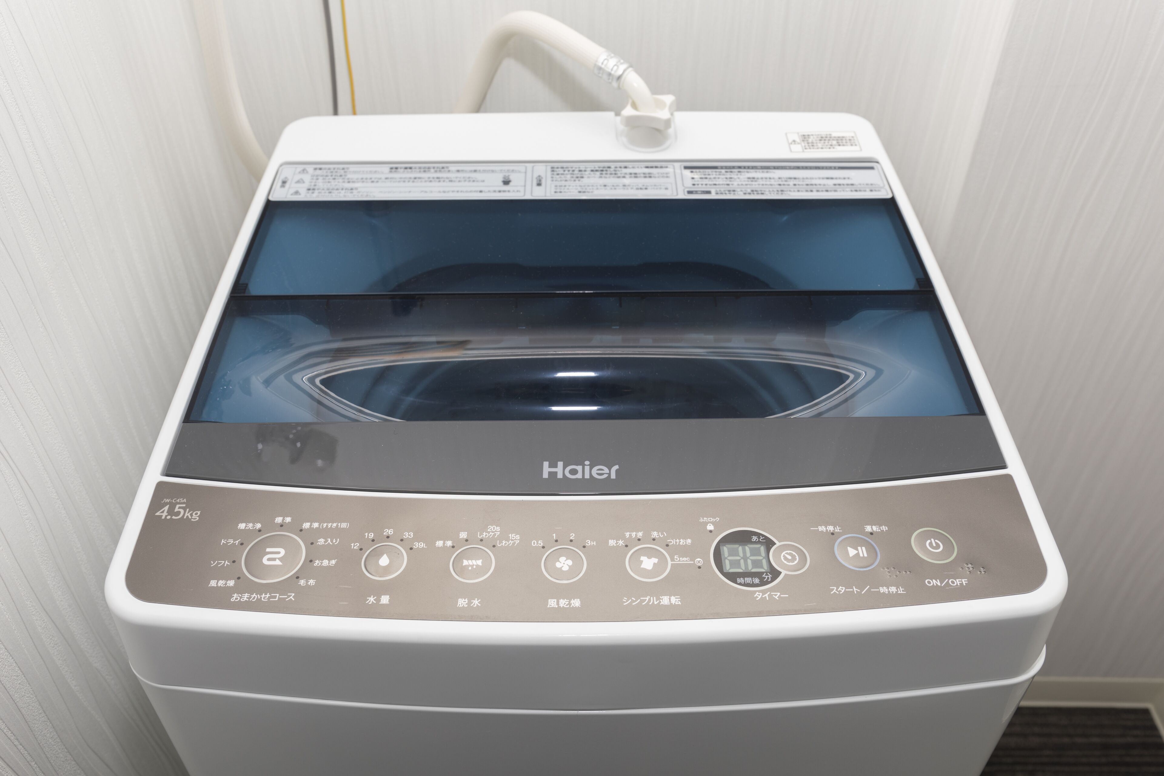 Una lavadora Haier con puerta transparente, panel de control y manguera de entrada de agua.