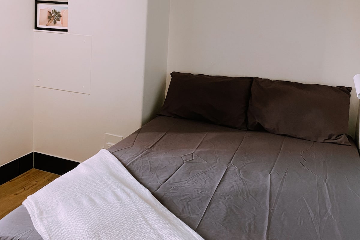 Un dormitorio con cama, almohadas, una colcha y un cuadro en la pared.