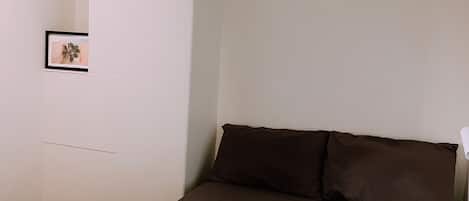 A bedroom with a bed, pillows, a blanket, and a framed picture on the wall.