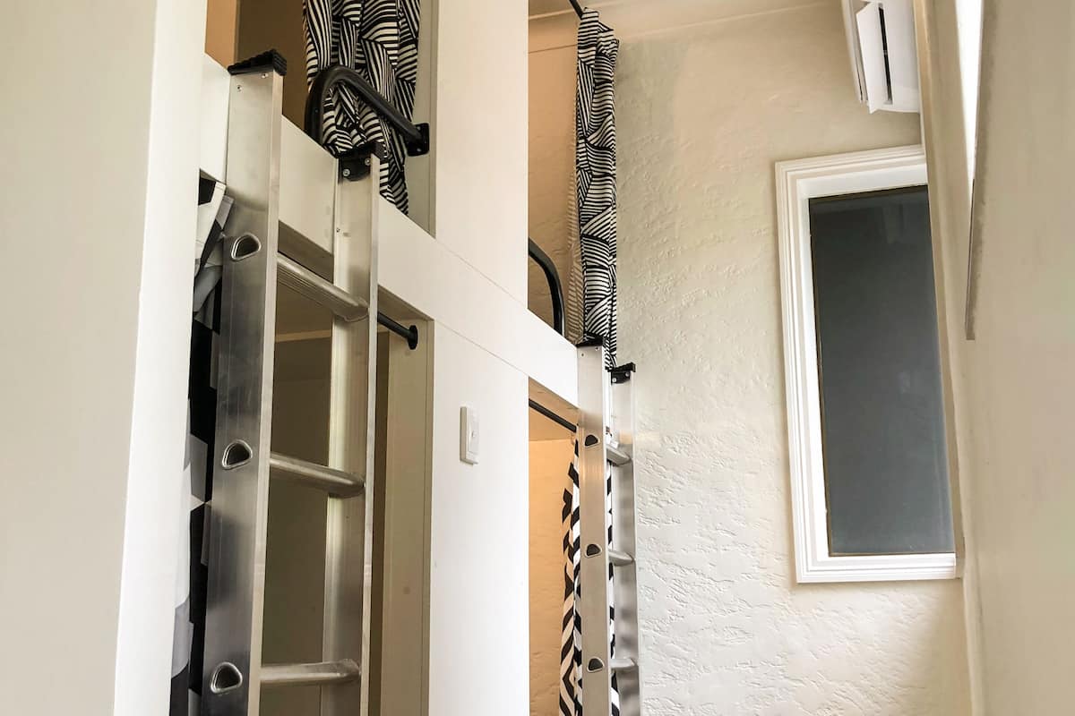Un pasillo estrecho con una escalera metálica, un ventanal con una persiana y una puerta con un cortinero a rayas de cebra.
