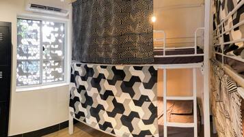 A bunk bed with geometric patterned bedding, a window with a geometric window screen, and a black metal locker.
