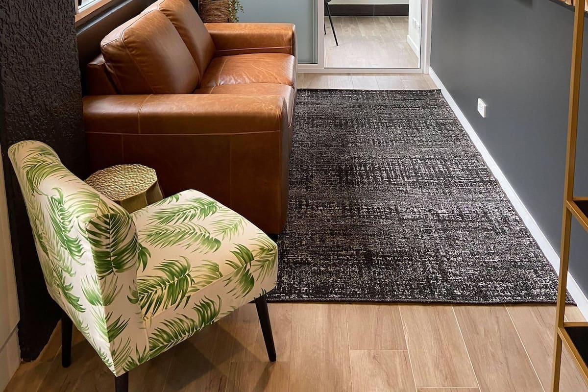 Una sala moderna con un sofá de cuero, un sillón estampado, un tapete texturizado negro y un televisor montado en la pared.