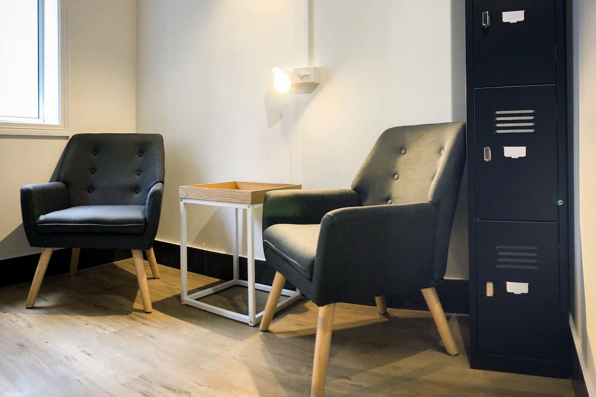 Una habitación con dos sillones negros, una pequeña mesa blanca y un archivador negro.