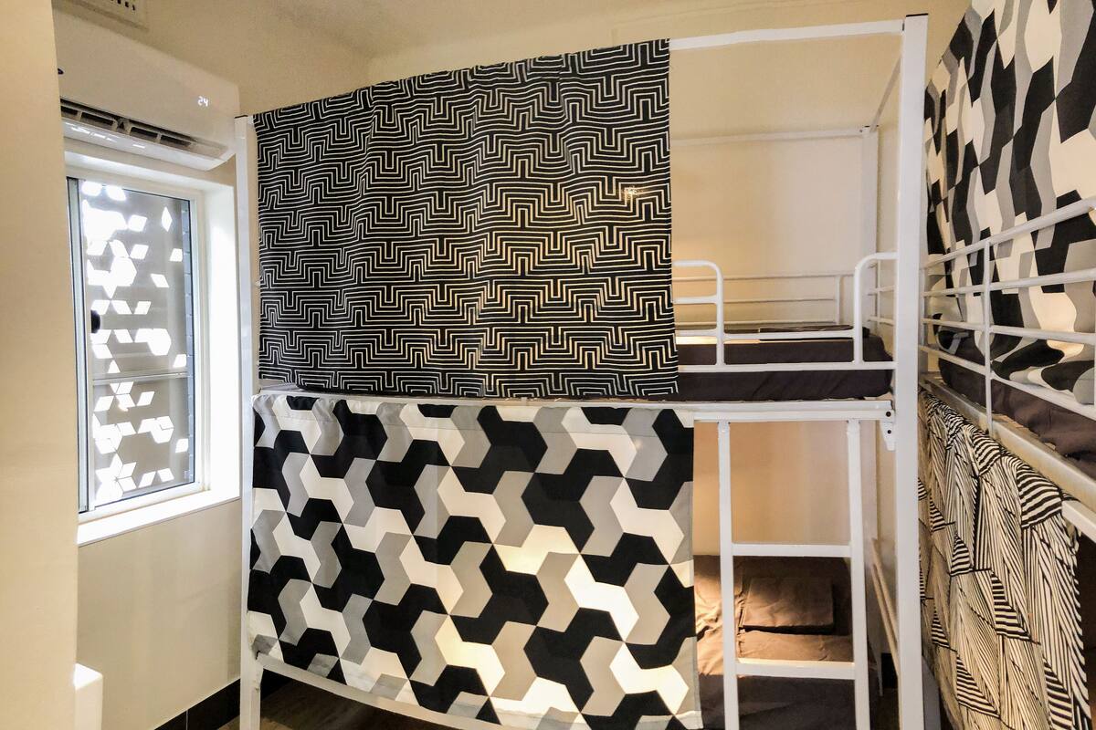 Una cama litera con ropa de cama de diseño geométrico, una ventana con persiana geométrica y una pared decorada.