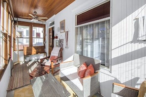 Ein sonnendurchflutetes Zimmer mit Deckenventilator aus Holz, Korbmöbeln und großen Fenstern.