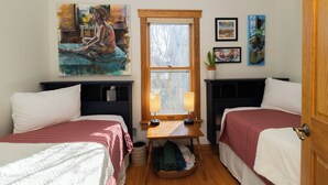 Une chambre avec deux lits, une fenêtre, un tableau et une petite table avec des lampes.