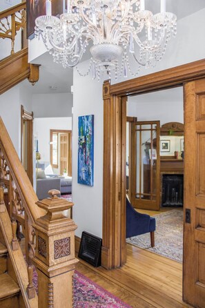 Un magnifique escalier, orné d’un lustre, avec des portes en bois et un tapis aux couleurs vives.