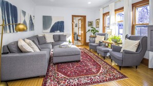 Un salon moderne avec des canapés gris, un tapis à motifs rouges et de grandes fenêtres ornées de rideaux blancs.