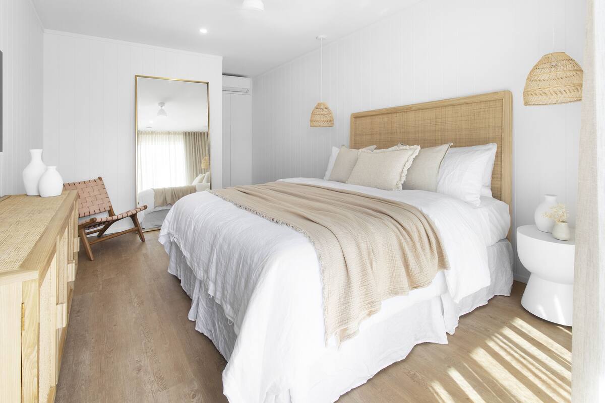 Une chambre à coucher moderne avec un grand lit, une table de chevet en bois, un miroir et une chaise en osier.