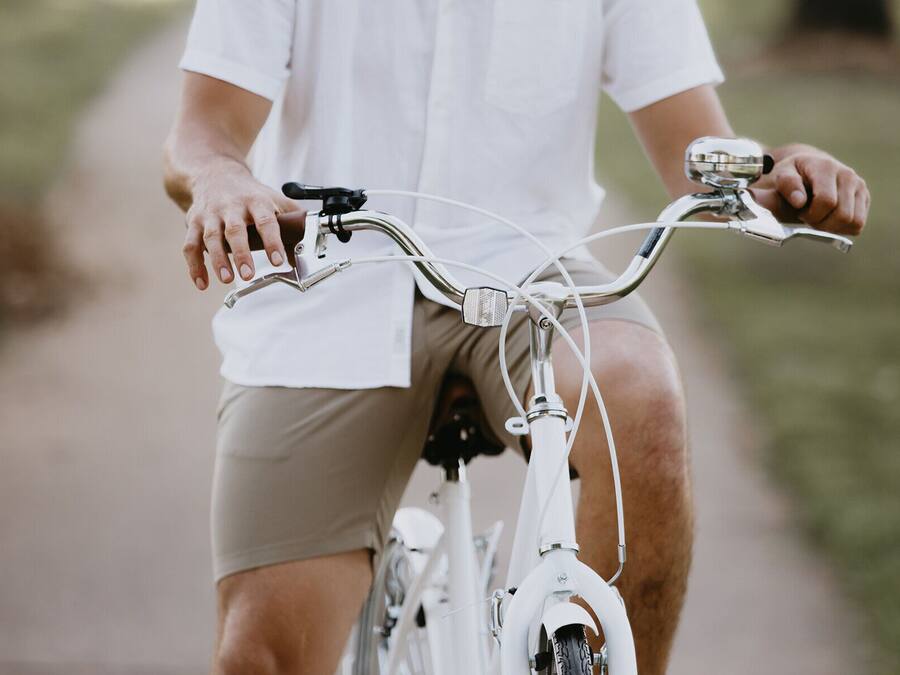A person riding a white bicycle with a white shirt and beige shorts.