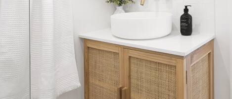 Un baño con lavamanos blanco, espejo redondo y mueble de madera con panel frontal tejido.