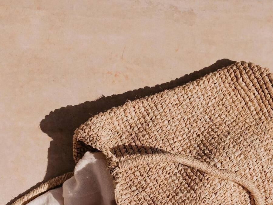 Un bolso tejido y un objeto blanco sobre una superficie rugosa.
