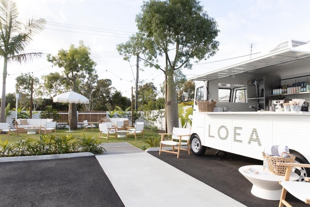 Un camion-restaurant blanc, arborant le logo « LOEA », est stationné dans un espace extérieur bien aménagé, agrémenté de sièges et de verdure.