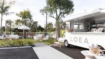 Un camión de comida blanco con la marca "LOEA" estacionado en un área exterior bien cuidada, con mesas y plantas.