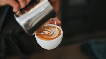 A person pouring steamed milk into a cup of coffee, creating a latte art design.