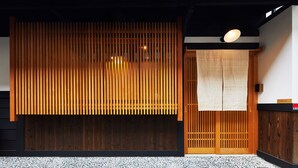 Een traditioneel Japans gebouw met een houten schuifdeur, een ingang van tatami-matten en een klein houten plankje met een bordje.