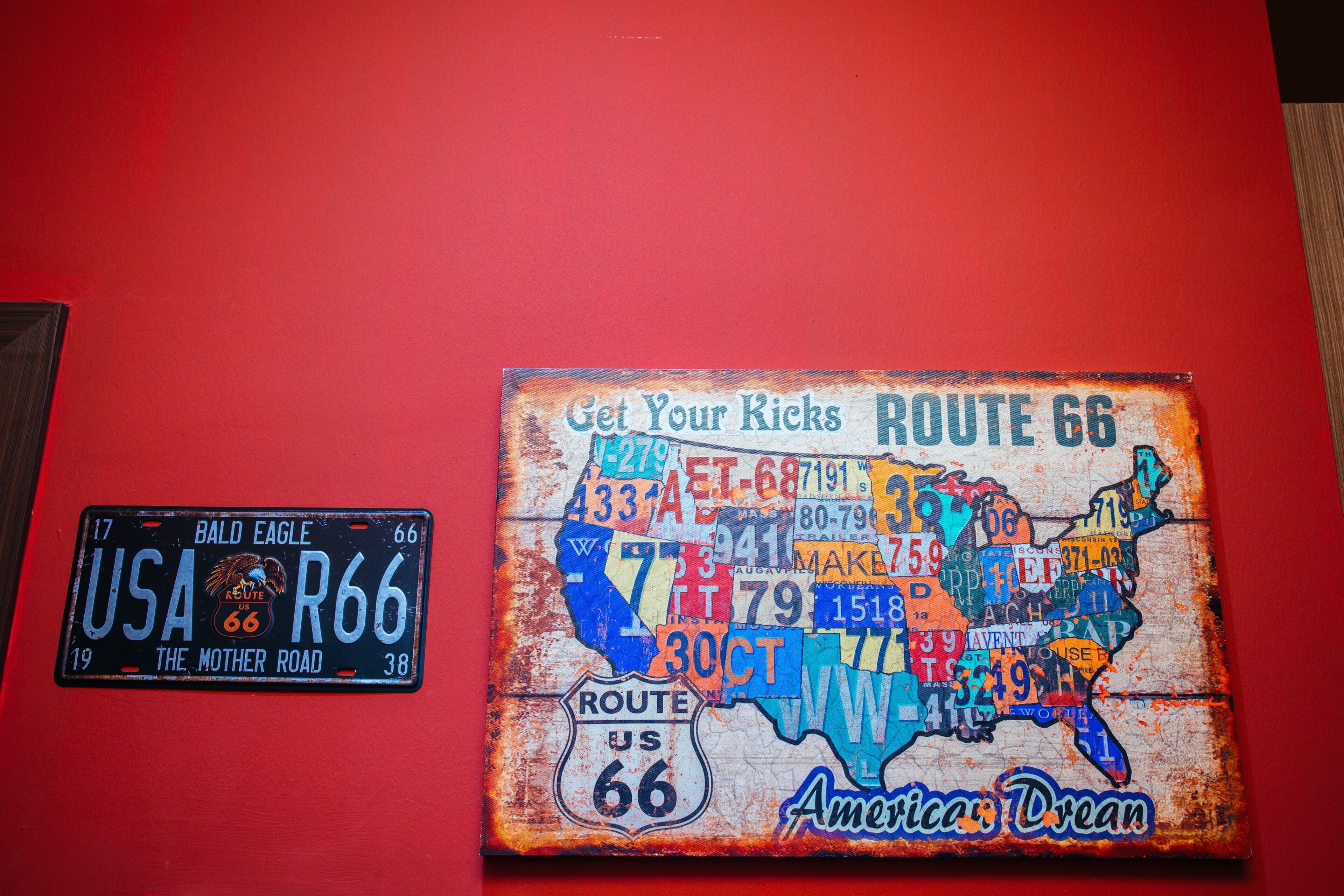 A Route 66 license plate and a Route 66 map mural on a red wall.
