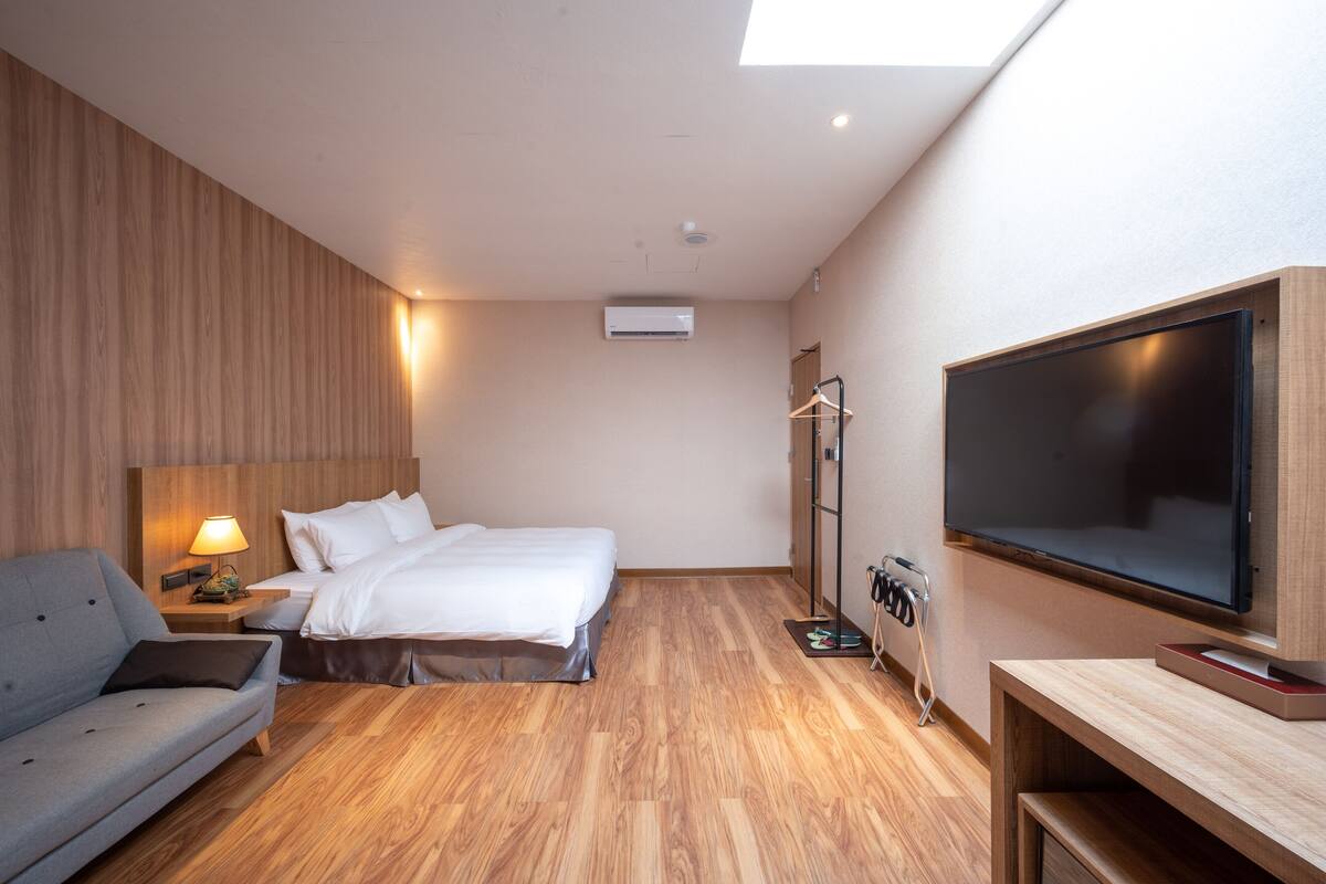 A hotel room with a bed, a sofa, a TV, and a wooden floor.