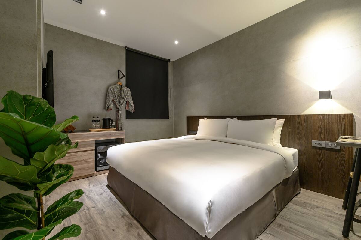 A modern bedroom with a large bed, a bedside table, a lamp, and a plant.