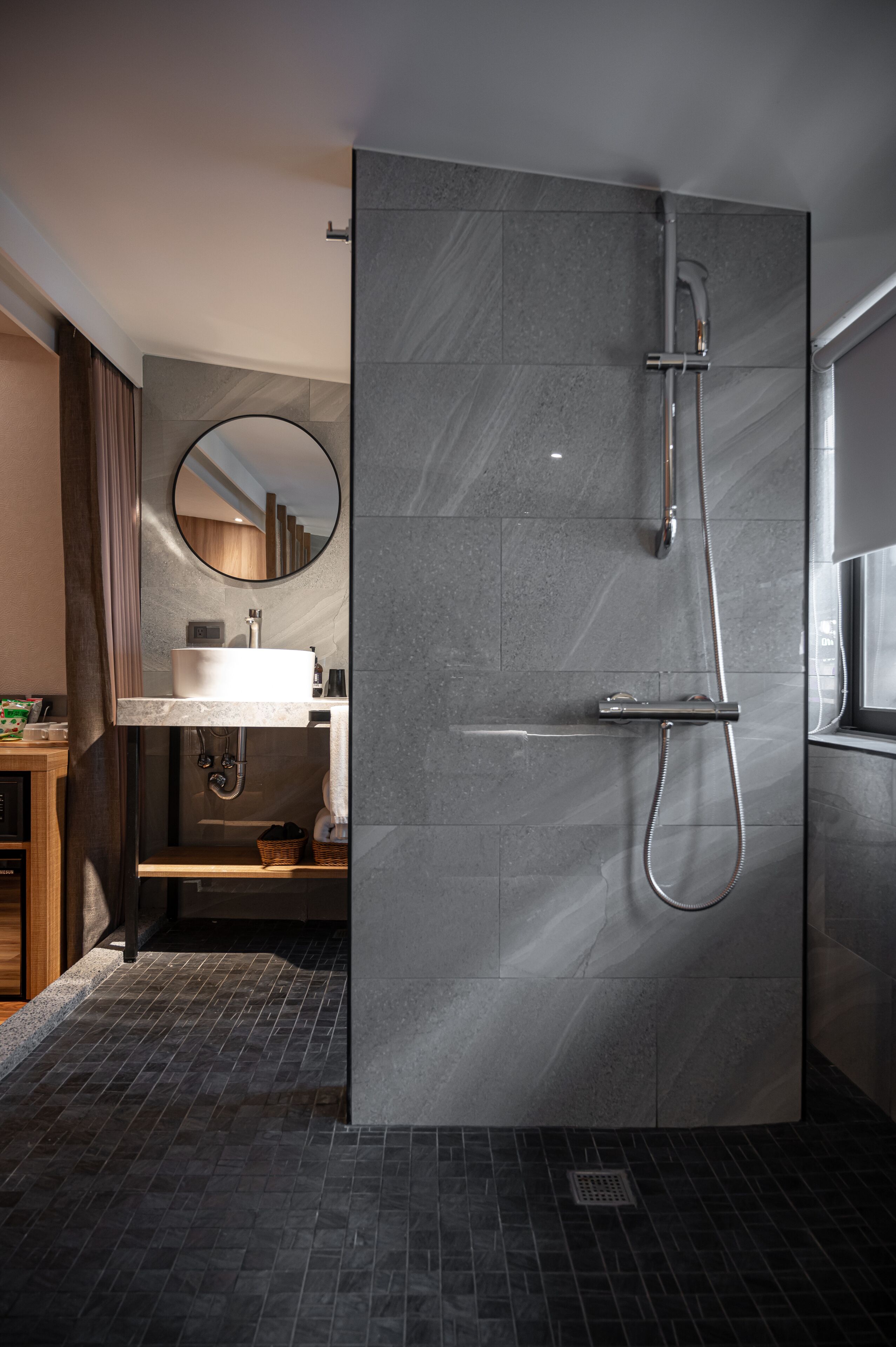 Ein modernes Badezimmer mit bodengleicher Dusche, rundem Spiegel und Waschbecken mit Marmorplatte.