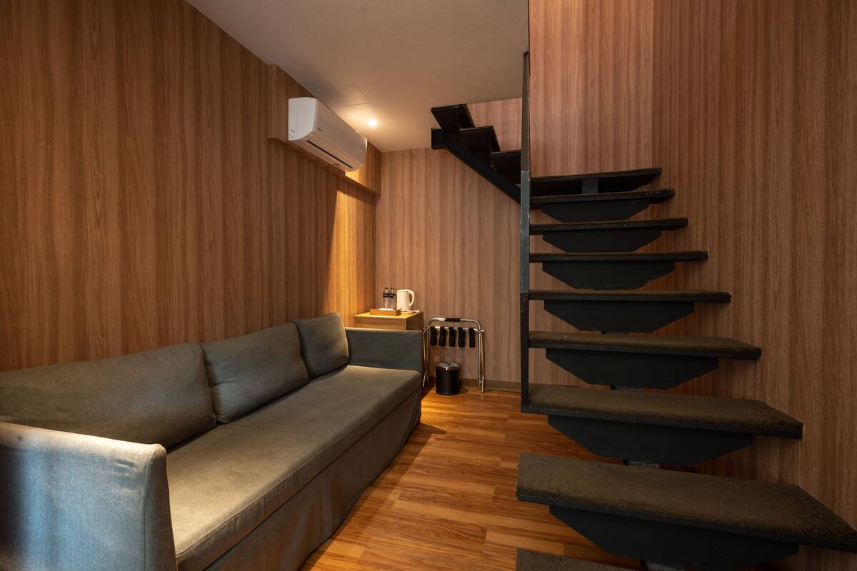 A modern interior with a wooden wall, a grey sofa, a staircase, and a coffee table.
