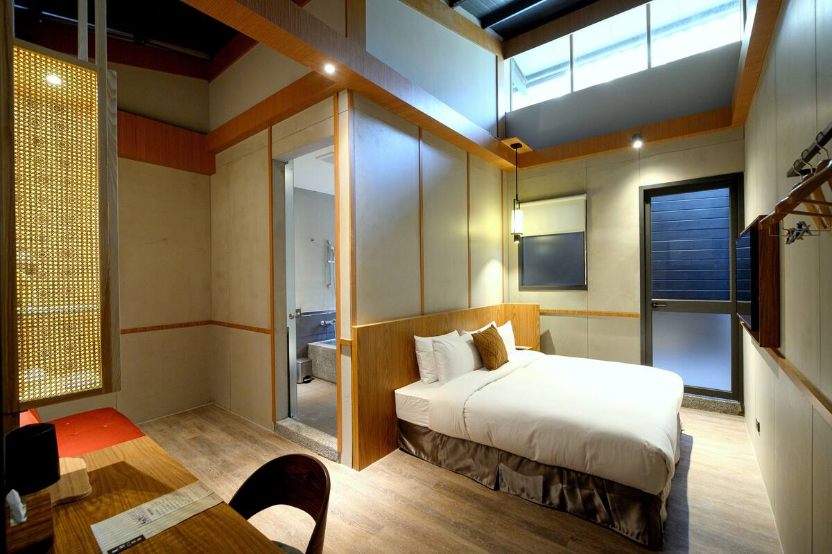 A modern hotel room with a large bed, a desk, and a view of the sky through a skylight.