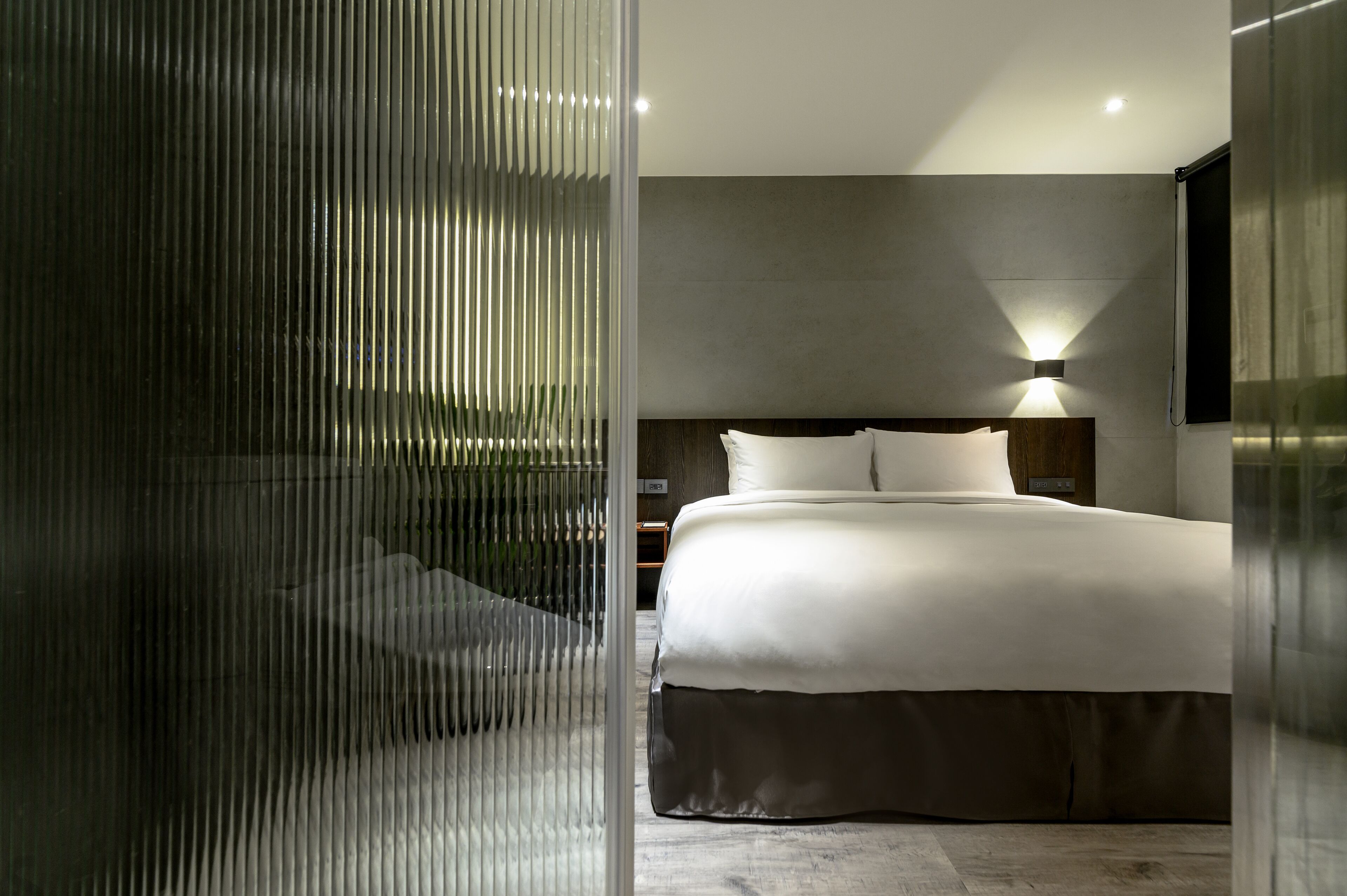 A modern bedroom with a large bed, a bedside table, and a wall-mounted light.