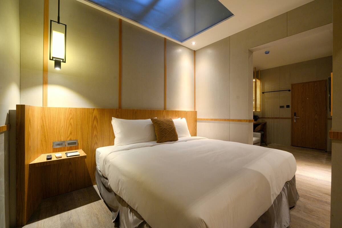 A modern hotel room with a large bed, wooden headboard, bedside tables, and a skylight.