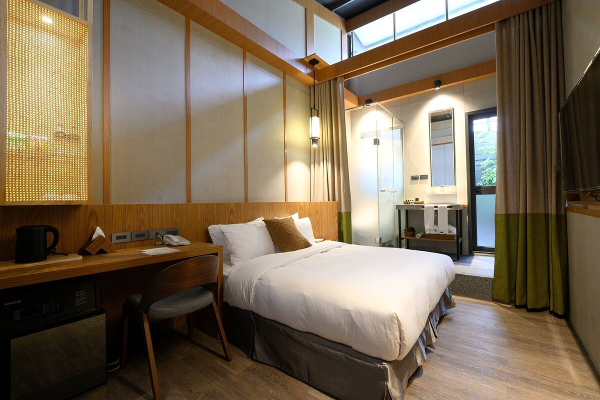 A hotel room with a bed, desk, chair, and a small kitchenette.