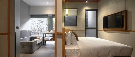 Un dormitorio moderno con una cama grande, una pared decorativa de piedra, un banco empotrado y un televisor montado en la pared.