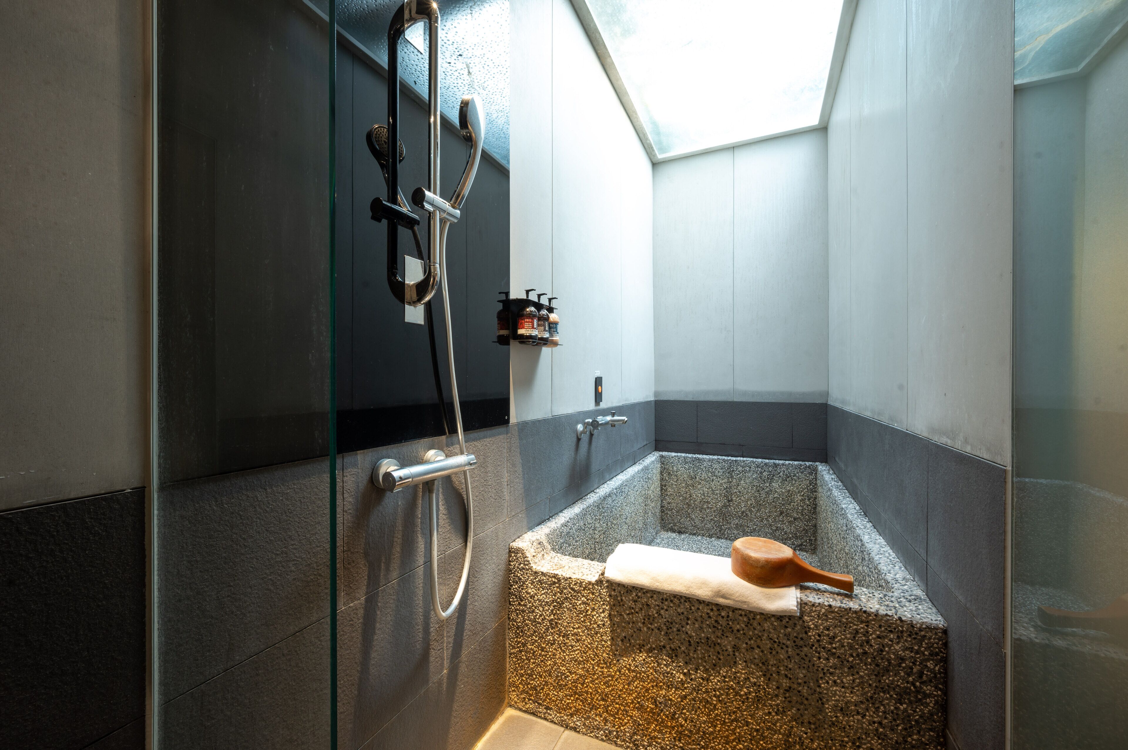 A modern bathroom with a glass-enclosed shower, a freestanding bathtub, and a skylight.