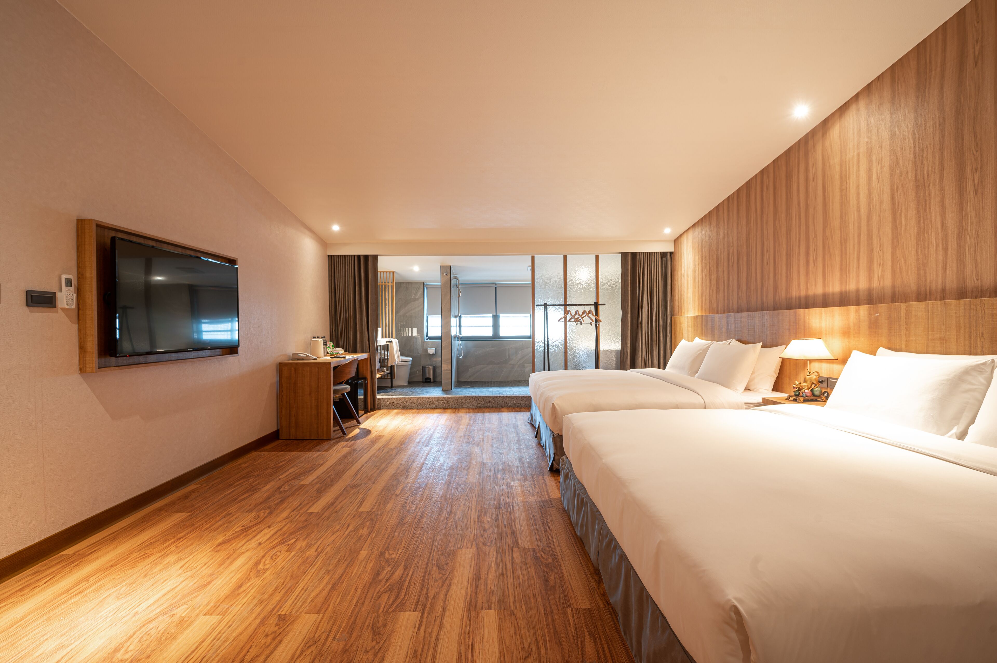 Habitación de hotel con una cama grande, un televisor montado en la pared, un escritorio con una silla y vistas al exterior a través de una puerta de cristal.