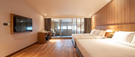Habitación de hotel con una cama grande, un televisor montado en la pared, un escritorio con una silla y vistas al exterior a través de una puerta de cristal.