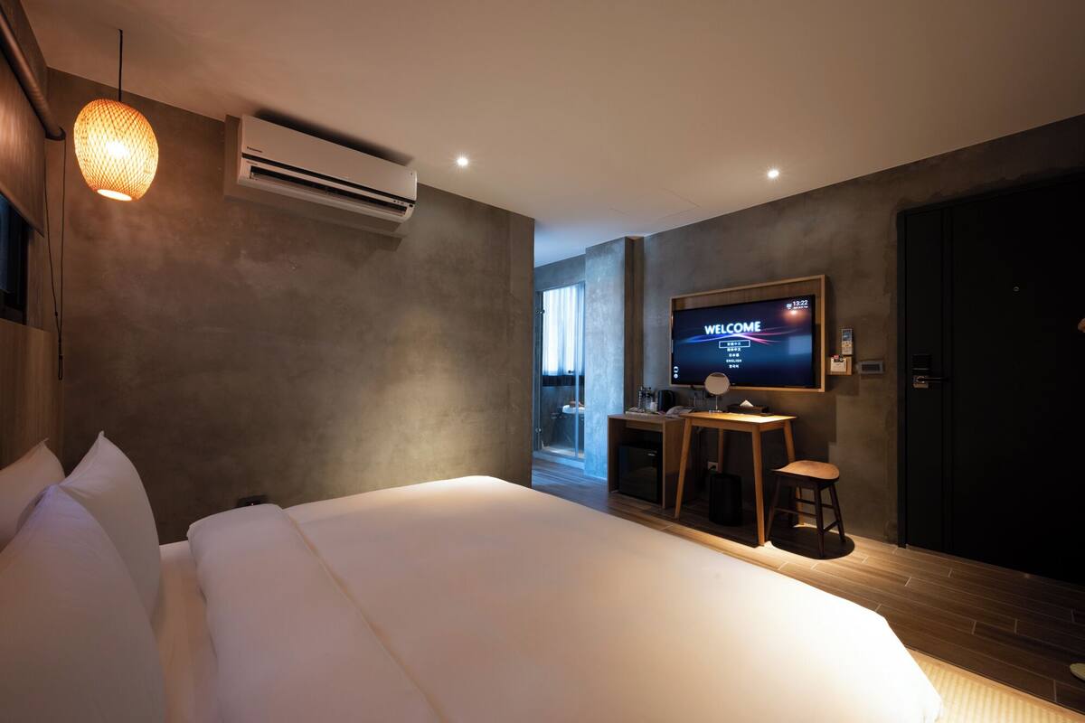 A modern hotel room with a large bed, a TV on the wall, and an air conditioning unit.