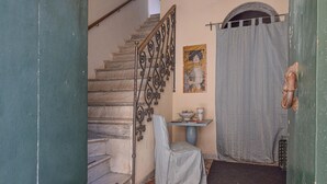 A staircase with ornate metal railings, a small table with a chair, a painting on the wall, and a partially open door with a curtain.