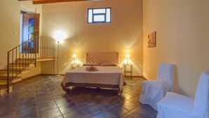 A bedroom with a bed, two bedside lamps, a chair, a small table, a window, and a staircase.