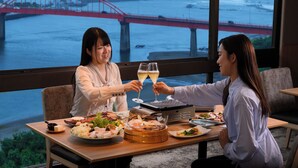 Una mesa de comedor con diferentes platos, una parrilla y vistas a un puente rojo sobre el agua.