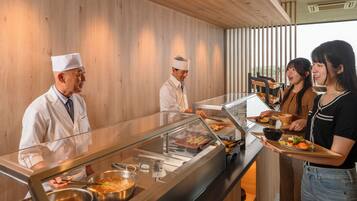 A buffet setup with a glass display case, serving staff, and customers.